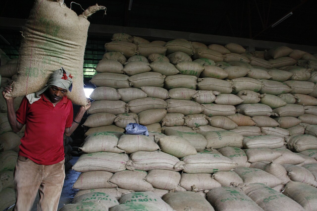 A worker carries a sack past thousands of stacked coffee bags in a warehouse
